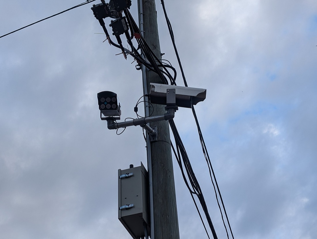 Two Leonardo ELSAG plate reader cameras bolted to an existing wooden utility pole, wired to a grey control box, alongside a separate infrared illuminator.